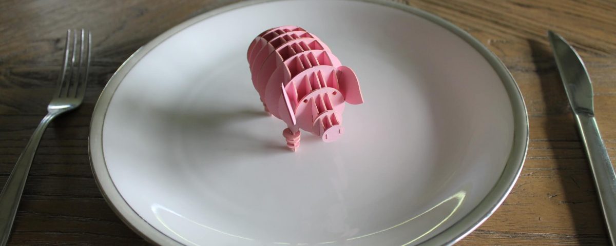 Pappschwein auf einem Teller mit Messer und Gabel
